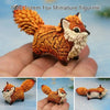 A hand-painted resin fox miniature figurine with an orange and white coat displayed in a person's palm.