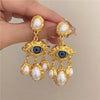 Gold vintage devil's eye pearl drop earrings featuring blue gemstone accents