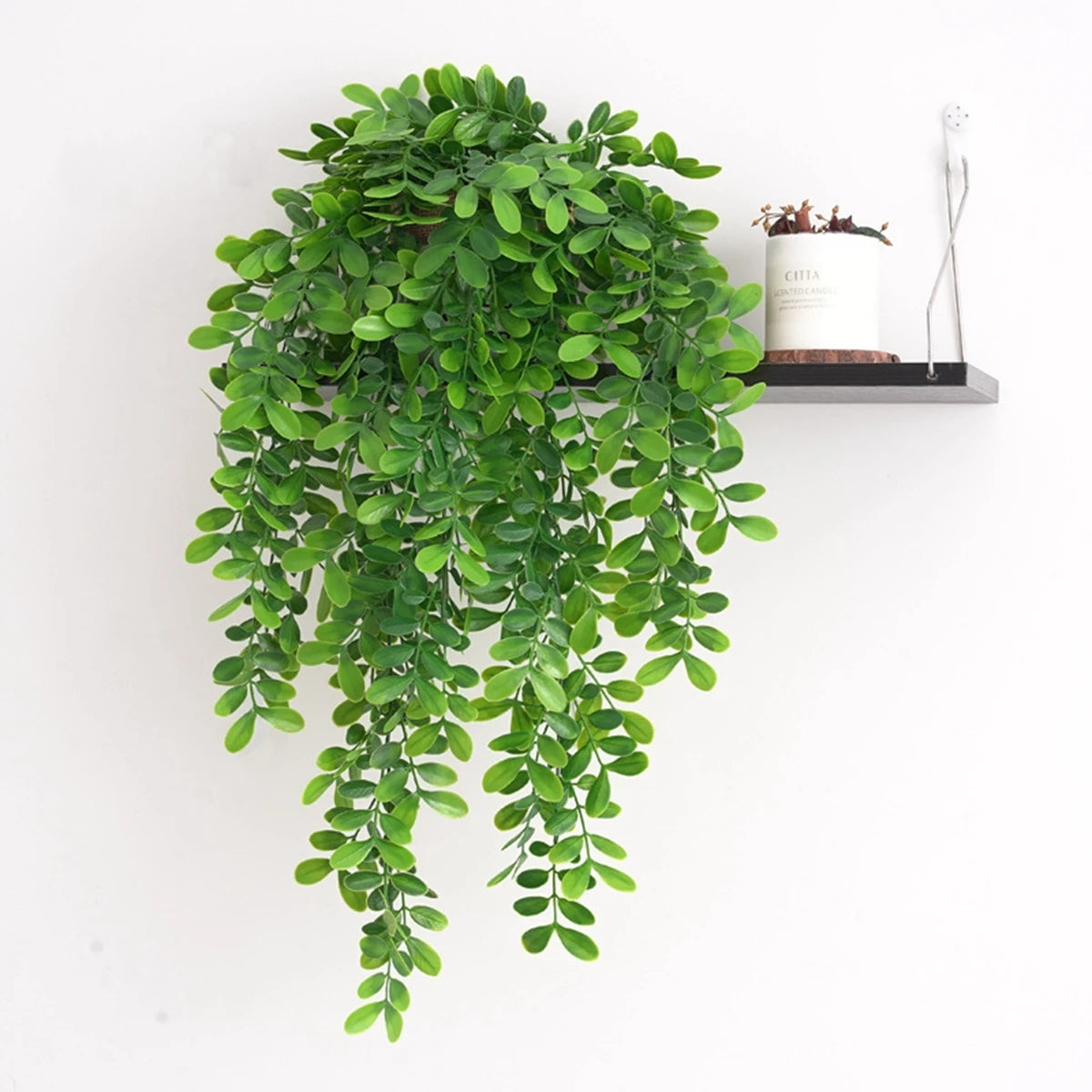 Artificial ivy vine cascading down a black shelf with a small candle and silver tool.