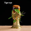 A brass chime shaped like a tree of life is decorated with green leaves and placed next to a brown glass object.