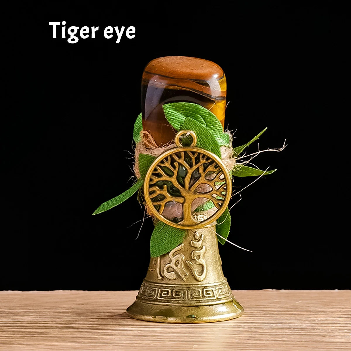 A brass chime shaped like a tree of life is decorated with green leaves and placed next to a brown glass object.