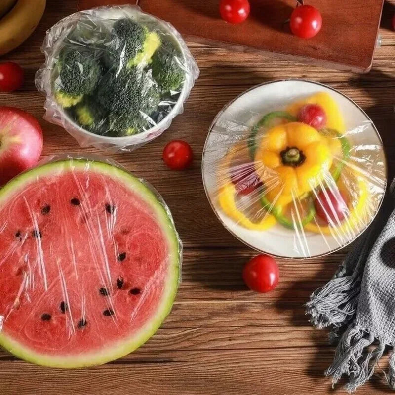 A flat slice of watermelon, a plastic bag of broccoli, and several small red tomatoes arranged on a wooden surface.
