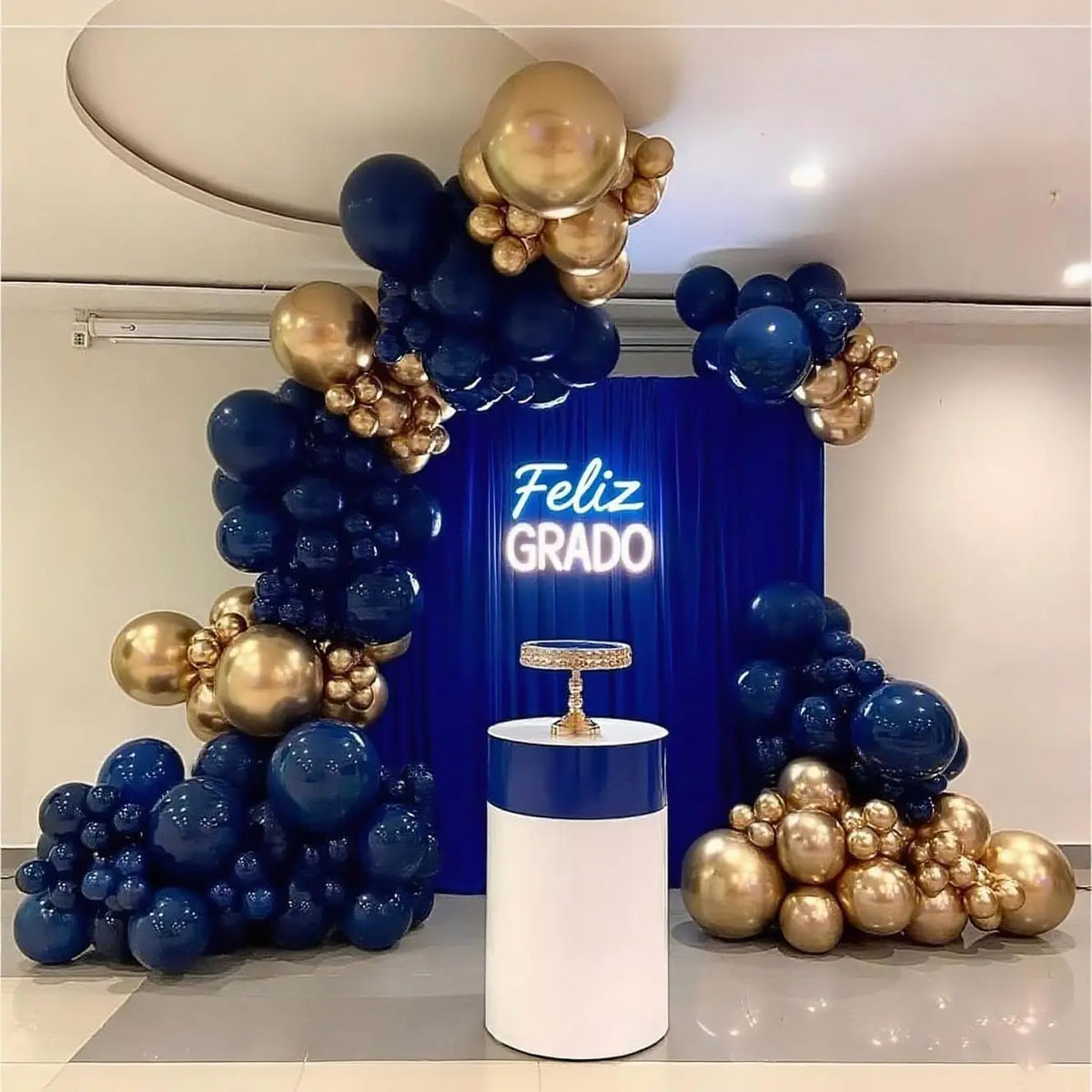 A balloon arch decoration featuring metallic gold and deep blue balloons with 'Feliz Grado' text.