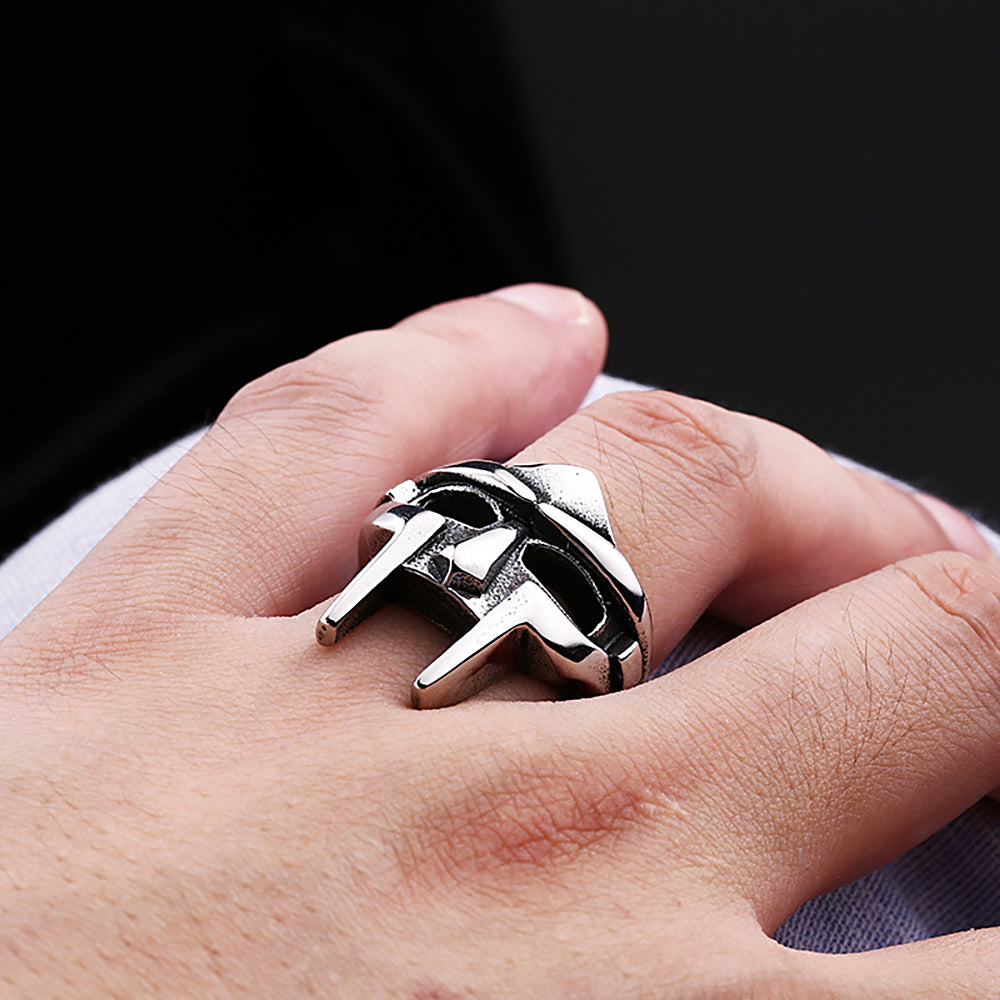 A close-up of a hand wearing a silver stainless steel ring shaped like an MF Doom mask.