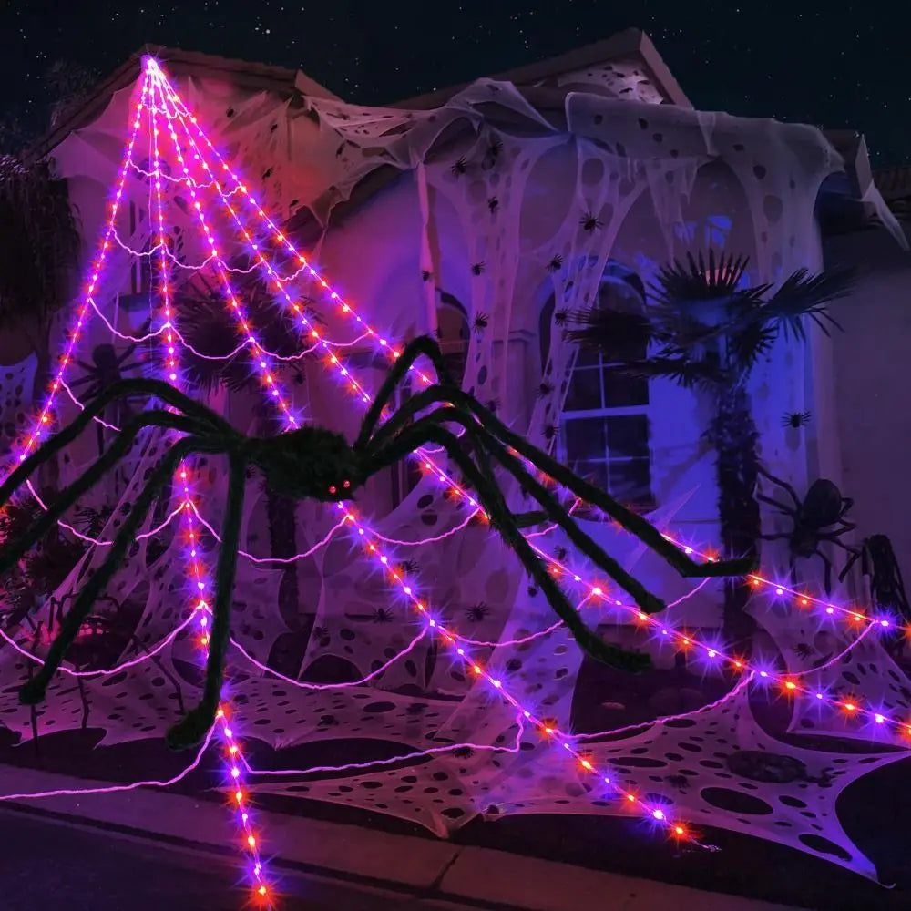 A giant spider web illuminated by purple and pink LED lights against a building facade at night.