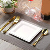 A set of gold-colored cutlery and a white square paper plate are displayed on a gray napkin with a glass of red wine in the b