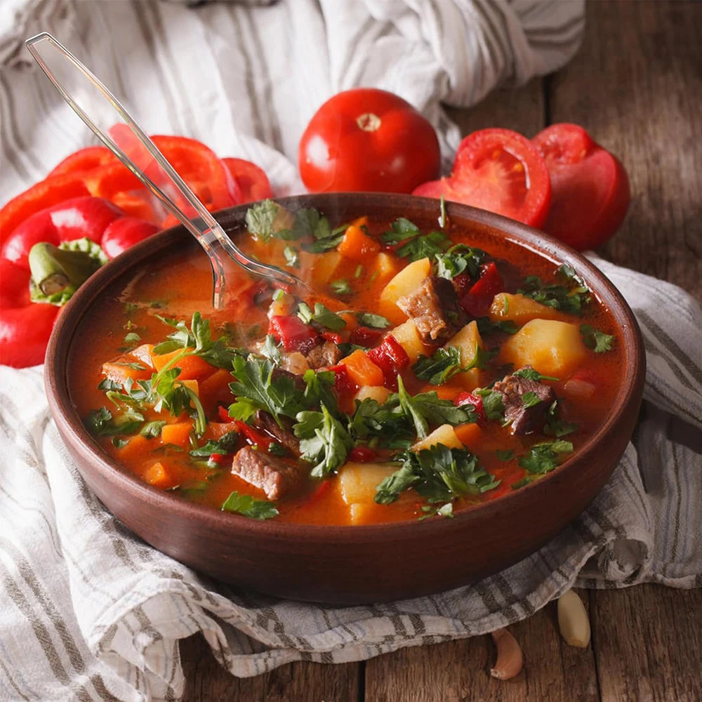 A bowl of hearty tomato soup garnished with herbs and served alongside fresh tomatoes.