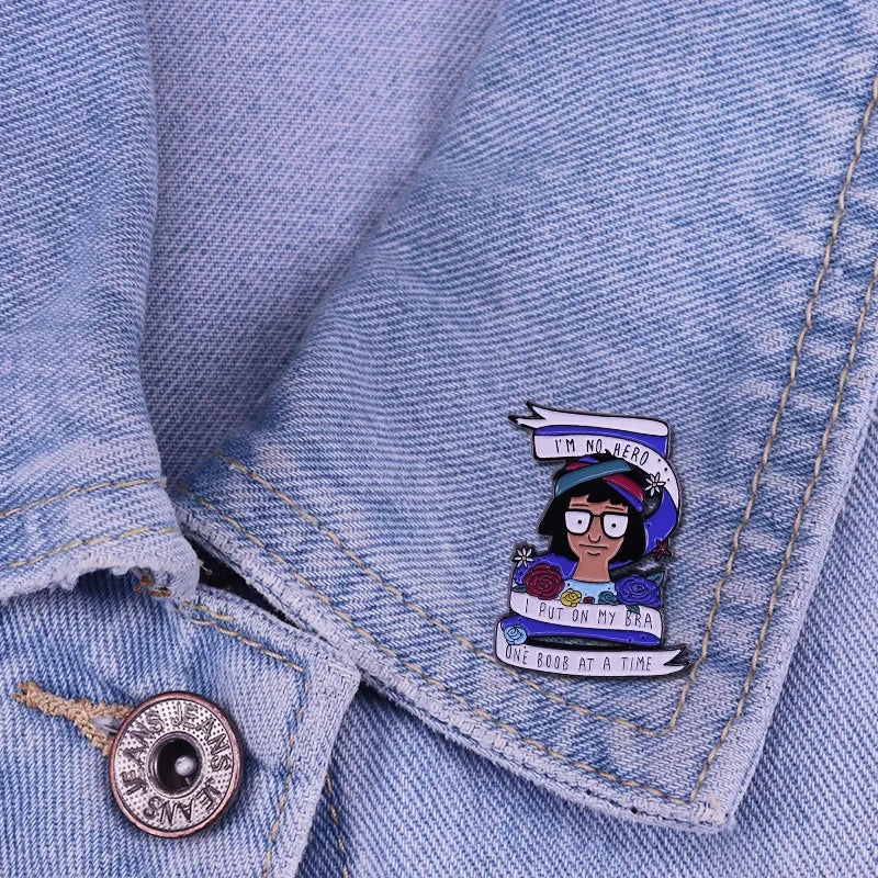 A blue denim shirt sleeve features an enamel pin badge depicting a cartoon character with text on it.