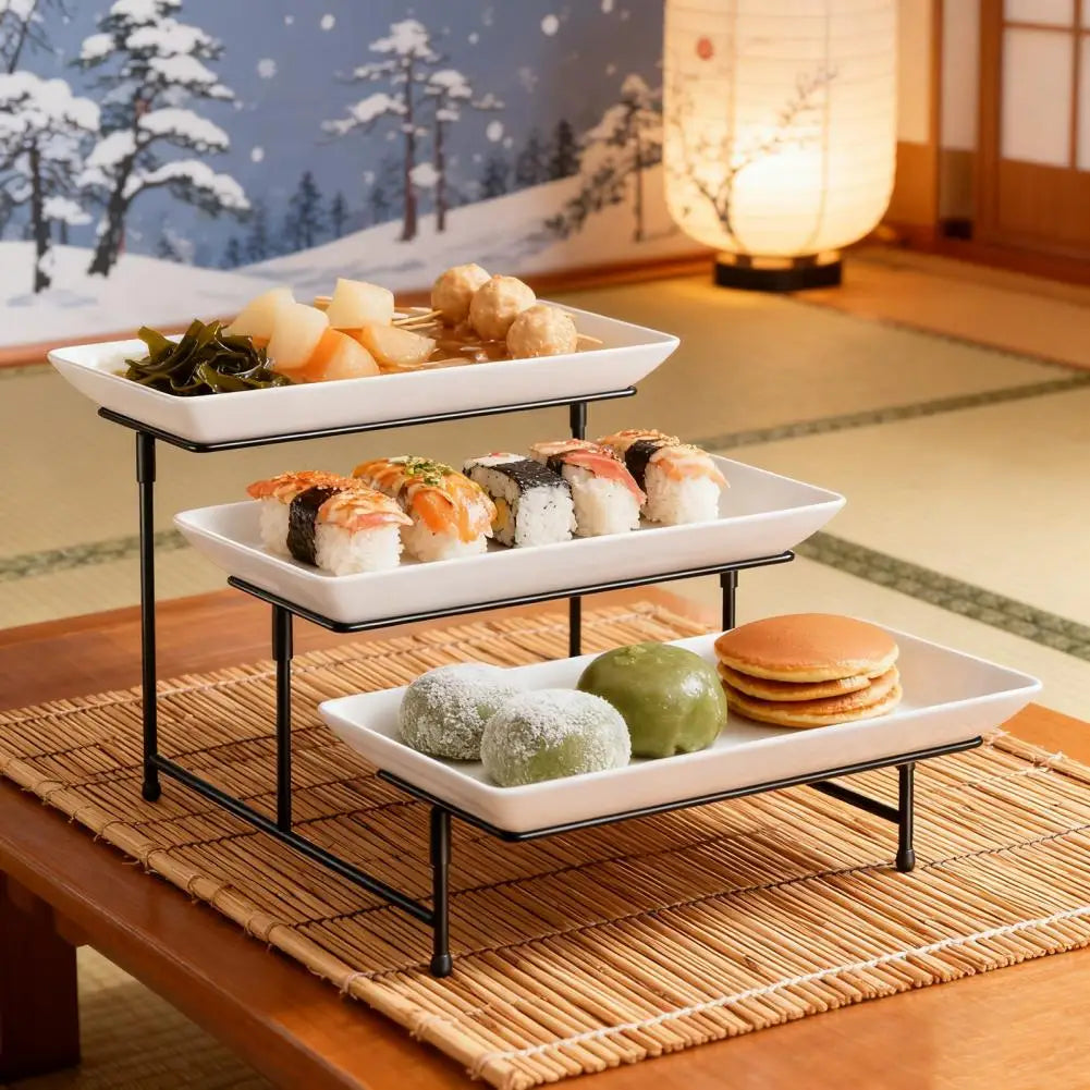An elegant three-tier serving rack displaying various Japanese and Asian appetizers on a wooden table.