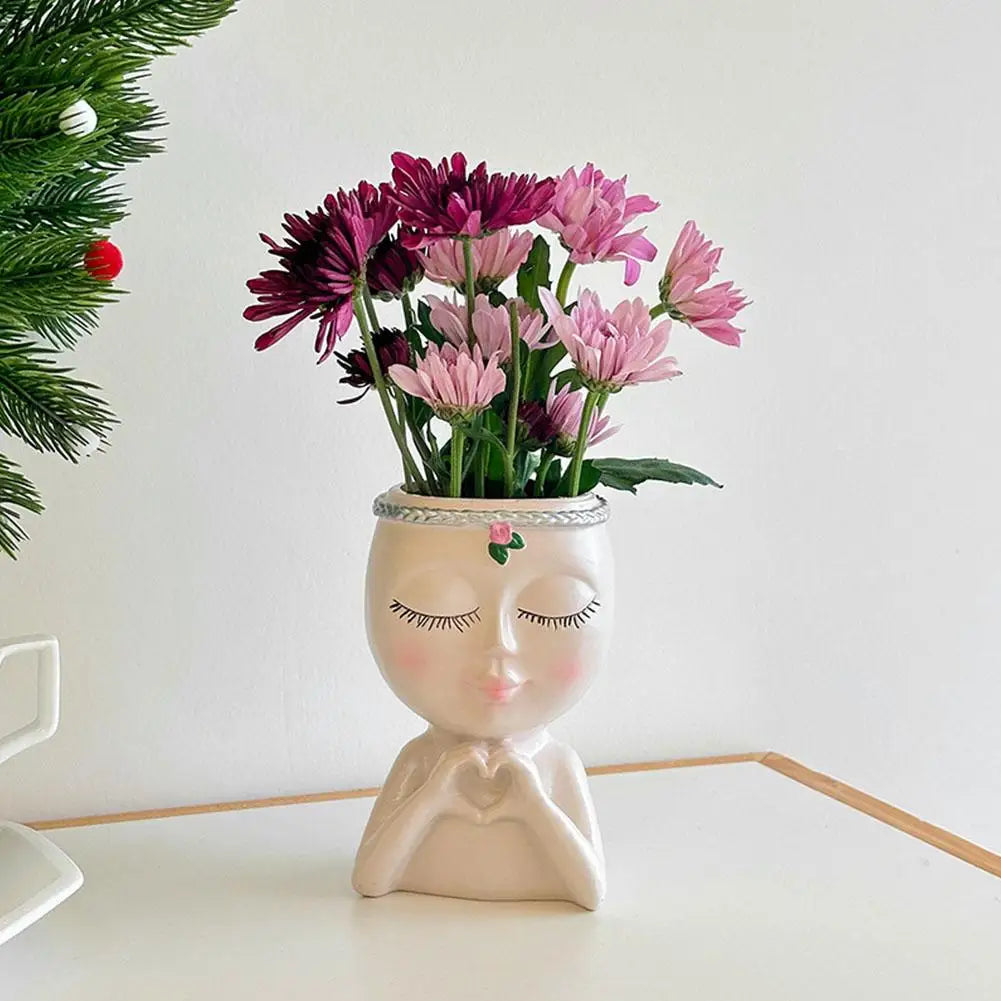 Artistic resin girl face planter with drainage hole holding pink and purple flowers.