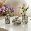 Three clear glass vases holding purple and pink flowers on a white surface.