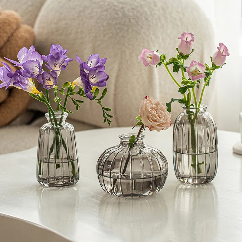 Three clear glass vases holding purple and pink flowers on a white surface.