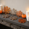 A collection of orange and natural wood wooden spider web ornaments displayed on a dark stone ledge next to white candles.