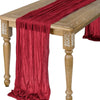 A deep red semi-sheer gauze table runner draped over a wooden table.