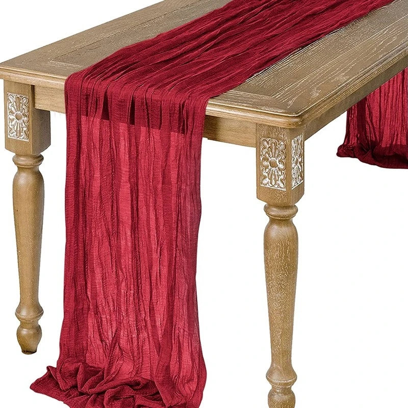 A deep red semi-sheer gauze table runner draped over a wooden table.