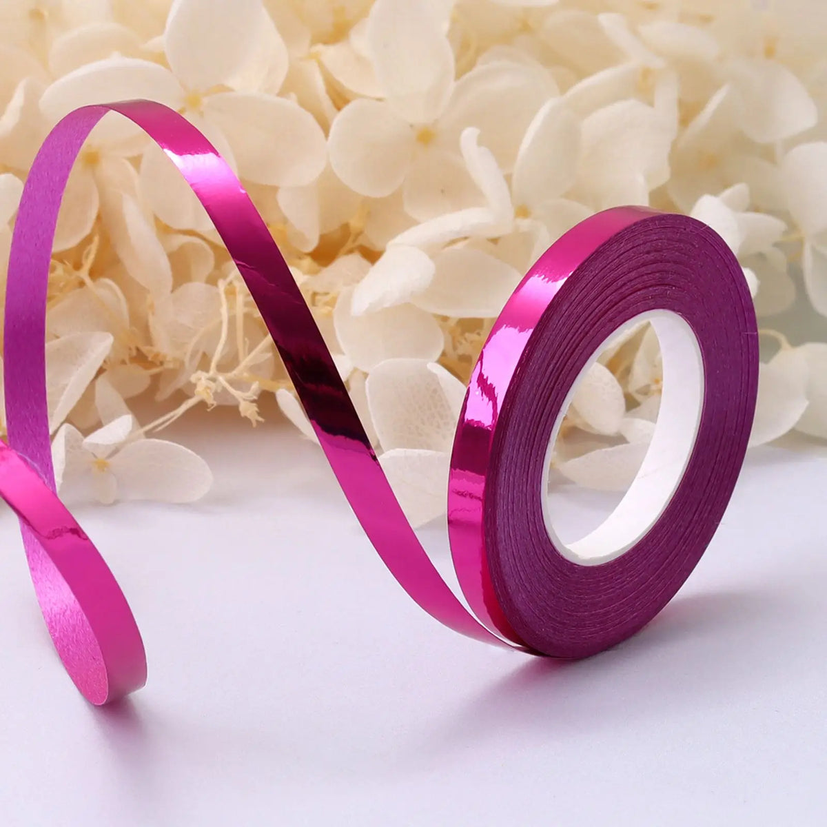 A roll of shiny purple satin balloon ribbon unwinding against a white background.