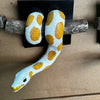 A wall sculpture of a ball python with white and yellow spotted patterning, mounted on a wooden stick.