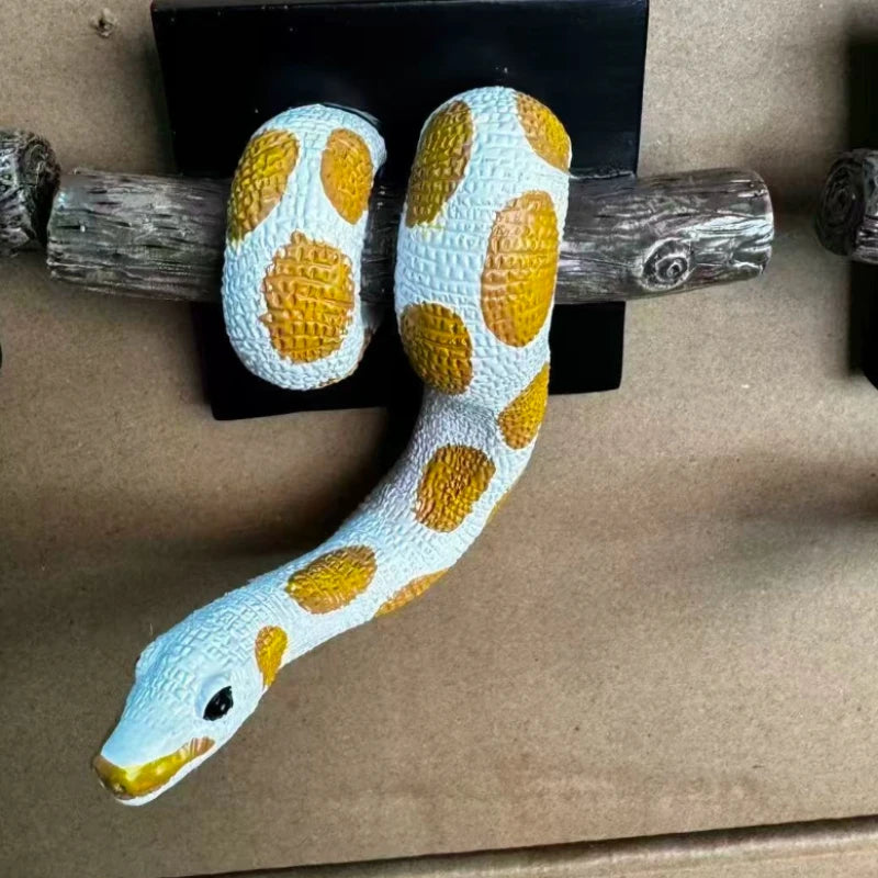 A wall sculpture of a ball python with white and yellow spotted patterning, mounted on a wooden stick.