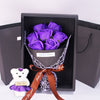 A gift box containing a purple rose bouquet and a white plush bear, tied with a brown ribbon.