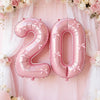 Pink foil number balloon shaped like 20 with bows, hanging against a pink and white floral backdrop.