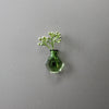 A small green glass vase holding delicate white sprigs of flowers mounted on a gray wall.