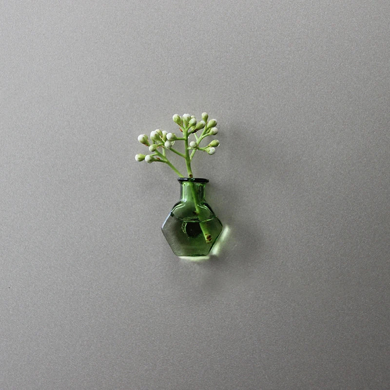 A small green glass vase holding delicate white sprigs of flowers mounted on a gray wall.