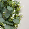 Green artificial eucalyptus leaves and small white flowers arranged for a wreath or decoration.