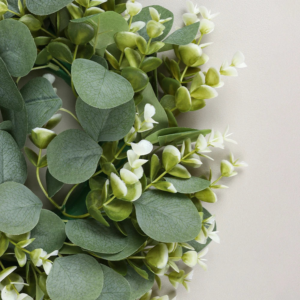 Green artificial eucalyptus leaves and small white flowers arranged for a wreath or decoration.