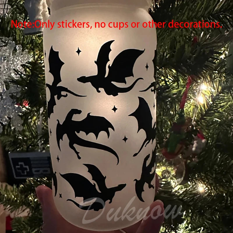 A hand holds a clear glass with black bat silhouette vinyl stickers for decoration.