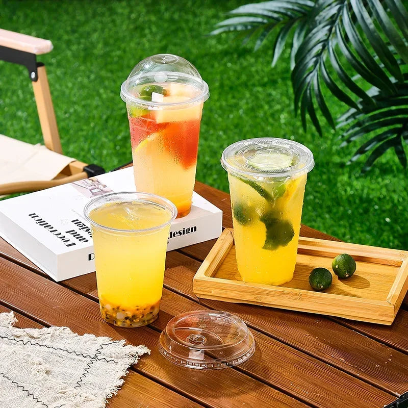 A collection of yellow and orange drinks in clear plastic cups with straws resting on a wooden table.