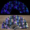 A folding fan with a dark background featuring vibrant purple and green UV fluorescent leaf patterns.