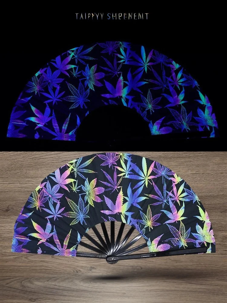 A folding fan with a dark background featuring vibrant purple and green UV fluorescent leaf patterns.