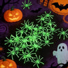 Glow-in-the-dark spider web Halloween decor featuring fake spiders and a carved pumpkin on a dark purple background.