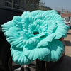 A large, light blue artificial peony flower displayed on a dark surface.
