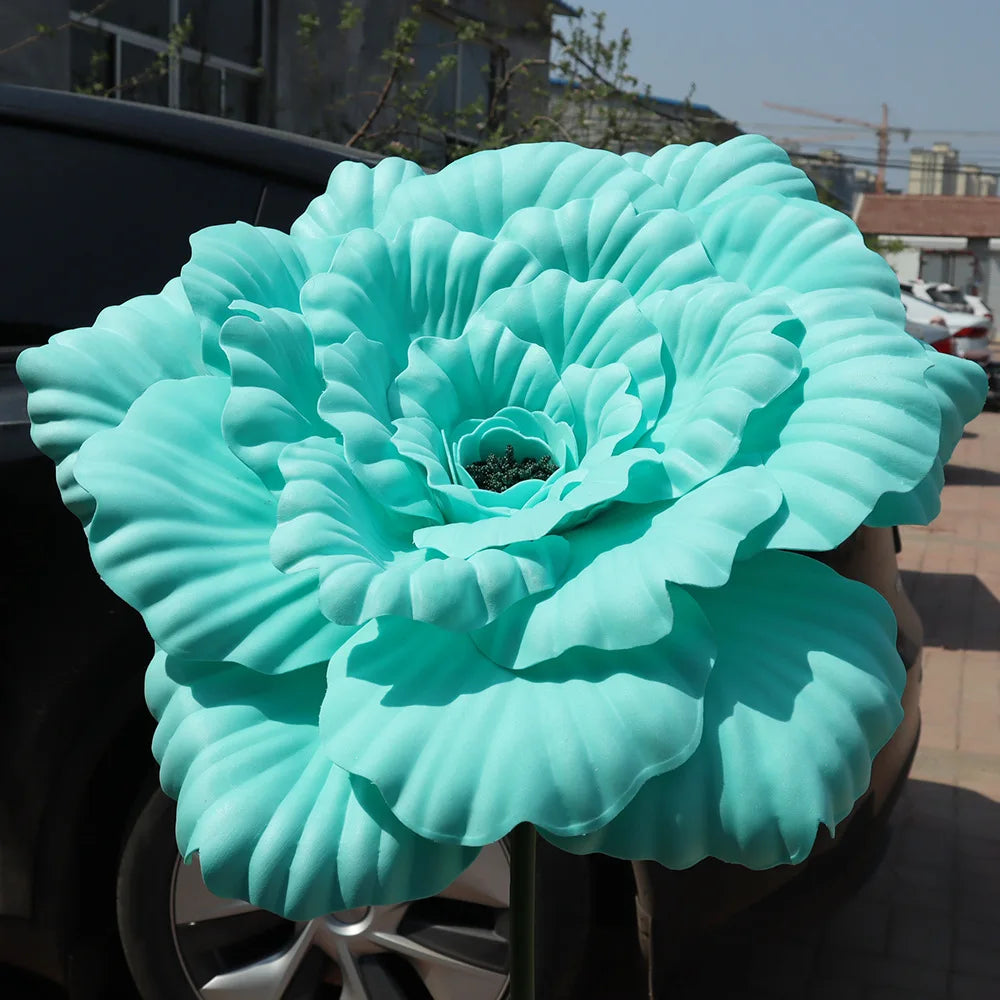 A large, light blue artificial peony flower displayed on a dark surface.