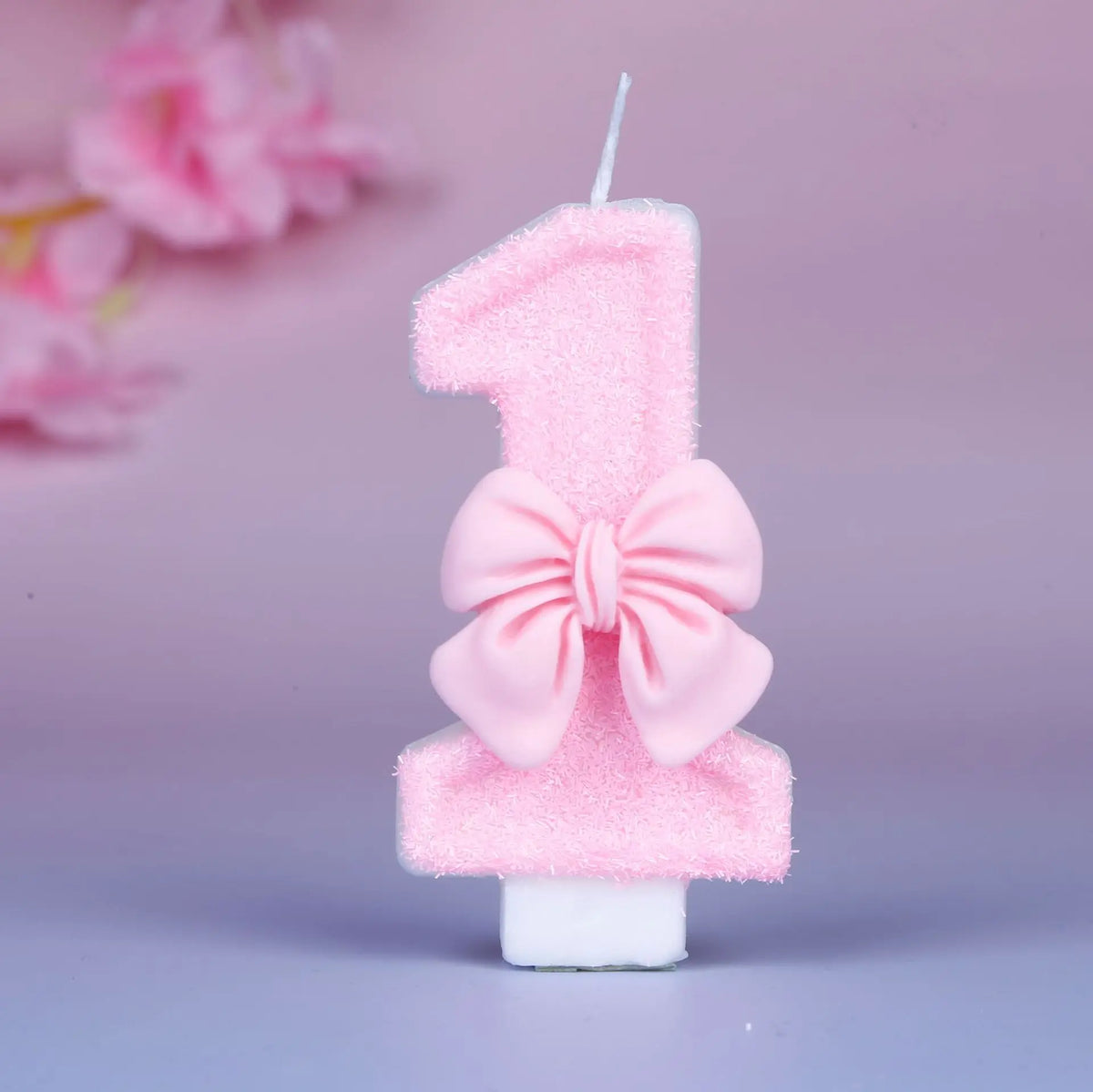 A pink glittery number one birthday candle decorated with a pink bow against a light purple background.
