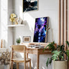 A framed poster of Gojo Satoru in a purple and blue aura hangs on a white wall next to a wooden desk.
