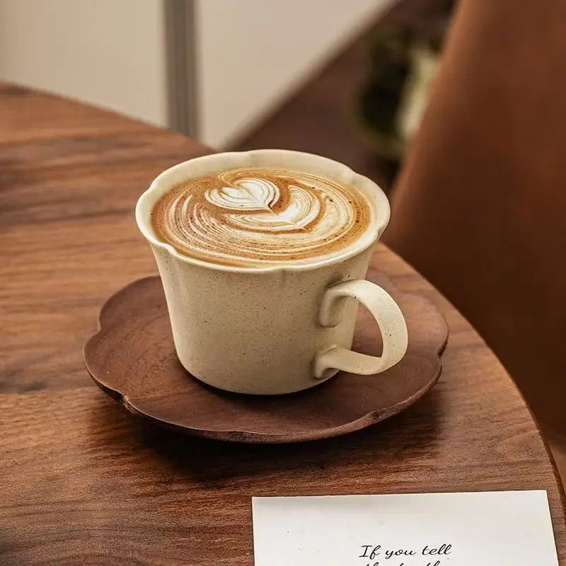 A latte art coffee in a ceramic cup and saucer set resting on a wooden table.