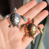 A pair of vintage marine life brooch pins featuring detailed turtle designs displayed on a hand.