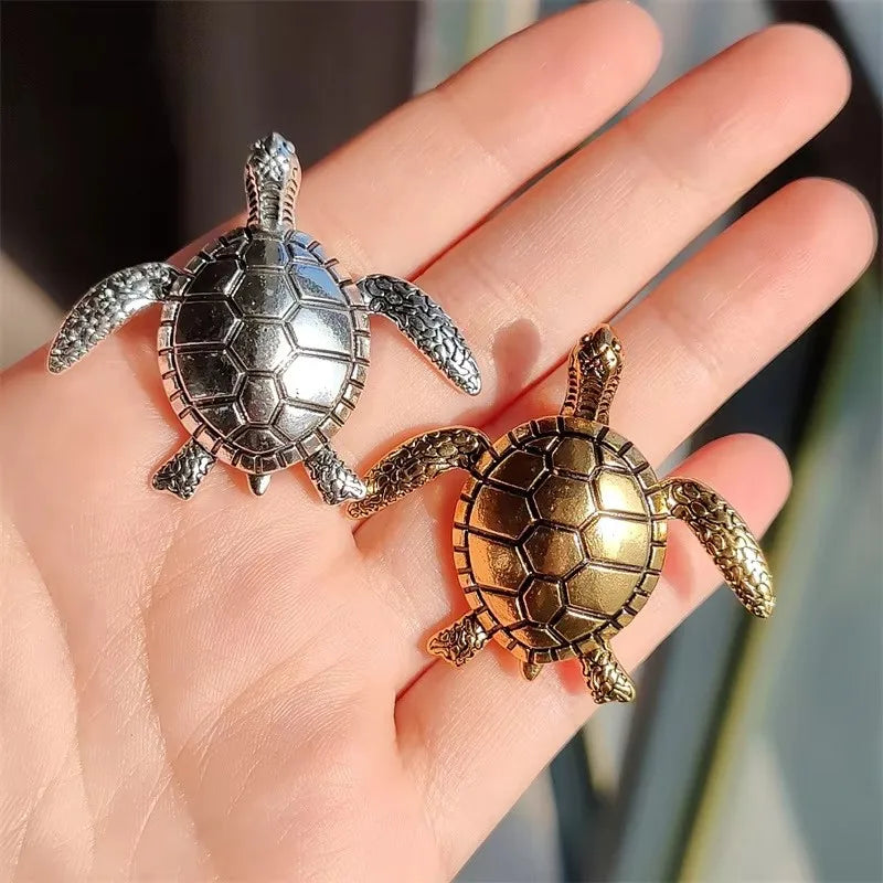 A pair of vintage marine life brooch pins featuring detailed turtle designs displayed on a hand.