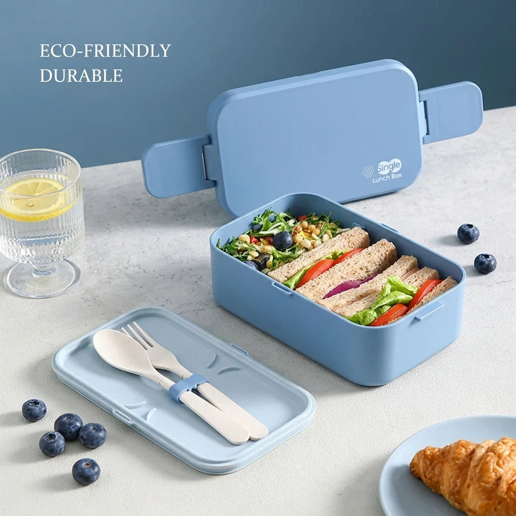A light blue eco-friendly bento lunch box is shown open, filled with food and accompanied by a set of wooden utensils.