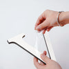 A hand holds a white acrylic letter wall sticker, demonstrating the size and shape of the self-adhesive decor.