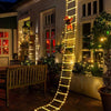 A golden string of Christmas lights forms a ladder decoration climbing up a white building facade.