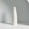 A tall, white ceramic vase with a tapered neck standing on a light surface.