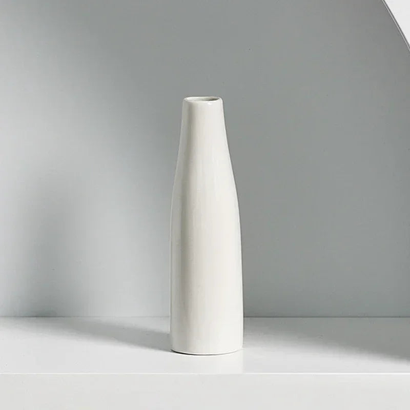 A tall, white ceramic vase with a tapered neck standing on a light surface.