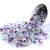 A pile of tumbled gemstone chips in various shades of purple and green crystals