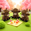 Three cute brown Highland cow statues with small orange food items on a yellow checkered mat