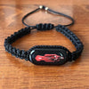A black braided leather bracelet with a rectangular pendant featuring a red vintage motorcycle.