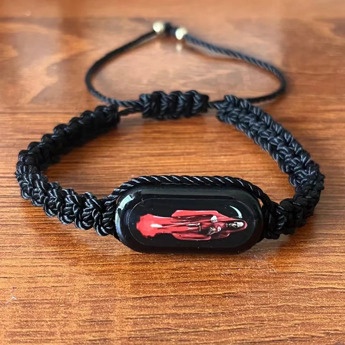A black braided leather bracelet with a rectangular pendant featuring a red vintage motorcycle.
