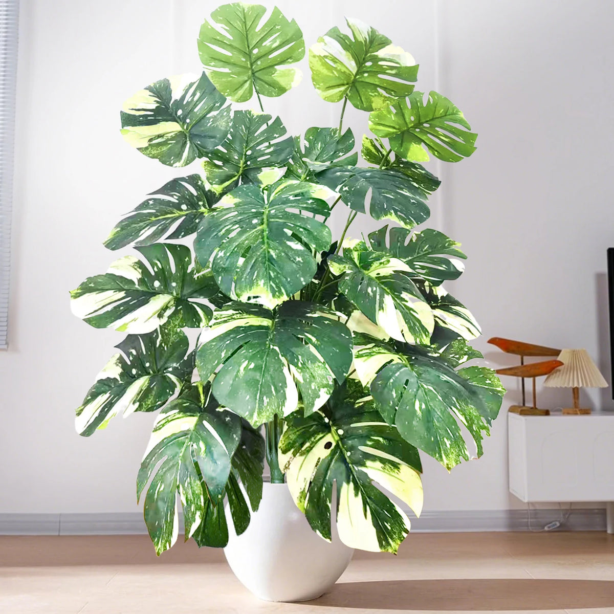 Artificial monstera plant with silk green and white leaves displayed in a white pot.